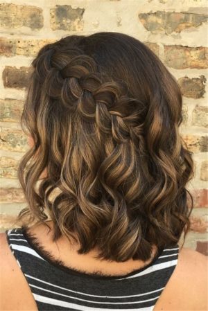 A Quinceanera with half up half down braids for short hair, standing in front of a brick wall.