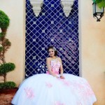 A woman in a Quinceanera dress sitting in front of a fountain with a beautiful design