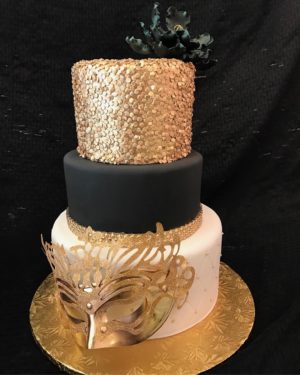 Quinceanera cake, a black and gold cake with a mask on top