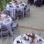 A group of tables set up for a formal Quinceanera event, featuring an elegant purple Quinceanera dress worn by a bridesmaid.