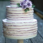 A three-tiered buttercream Quinceanera cake with purple flowers on top