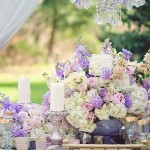A Quinceanera table with a bunch of lilac flowers and candles as a centrepiece