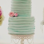 A Quinceanera cake with two tiers, decorated in mint green and pink. The top tier is adorned with pink roses.