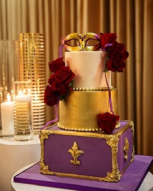 A purple and gold masquerade Quinceanera cake with a mask on top.