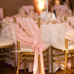 A table with a bunch of chairs covered in pink bows and chair sashes for chiavari chairs for a Quinceanera event.