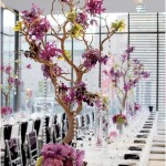 A Quinceanera-themed table centerpiece featuring a long table decorated with branches and a vase filled with flowers