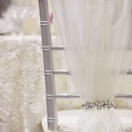 Quinceanera theme: Close up of a Chiavari chair with an organza sash on it, placed on a table.