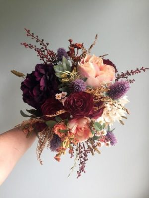 A person holding an artificial floral Quinceanera bouquet with autumn flowers in their hand