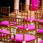 Rows of gold chairs with pink cushions in a Quinceanera function hall.