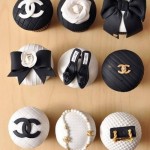 A table topped with cupcakes covered in black and white icing, including a cupcake designed to look like a Chanel logo made of marshmallow fondant