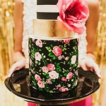 A woman holding a black and gold cake with floral print icing