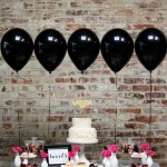 A Quinceanera party with a black theme. The table is covered in lots of desserts and balloons.