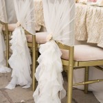 Quinceanera table set up with white ruffle chair covers and a bunch of chairs covered in white cloth
