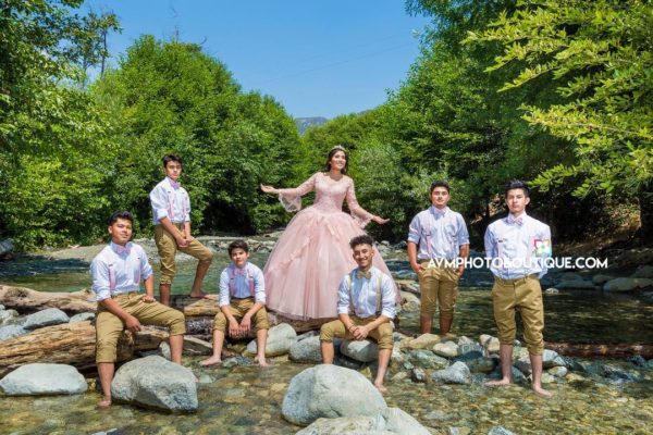 A group of people posing in front of a river during a Quinceanera photoshoot with a tree in the background