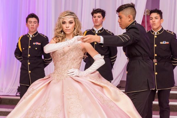 A lady Quinceañera, wearing a ball gown, dancing with a man in a military uniform