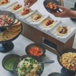 A Quinceanera soirée with a group of people standing around a table filled with plates of Taco food