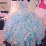 Two blue Quinceañera dresses displayed on mannequin stands in a room.