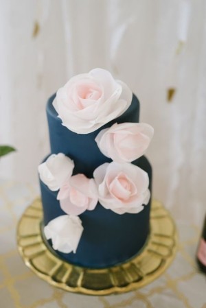 Close up of a navy, silver, white, and pink Quinceanera cake on a table, with a Quinceanera invitation nearby.