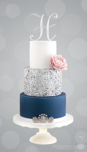 A Quinceanera themed silver sequin cake with three tiers and blue and white frosting.