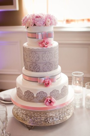 A Quinceanera cake with a gray and pink theme. It is a three-tiered cake with pink flowers on top.