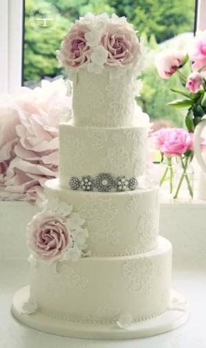 A three-tiered Quinceanera cake with lace and beading, adorned with pink roses