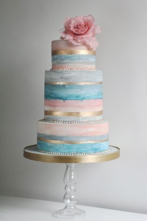 A pastel rose quartz and serenity Quinceanera cake. It is a three tiered cake with a pink flower on top.