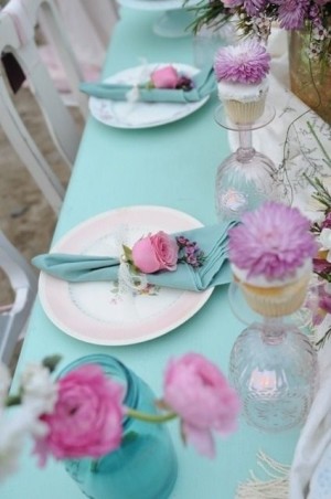 A Quinceanera table set with a lavender and aqua color scheme. The table is adorned with a blue table cloth and white plates.