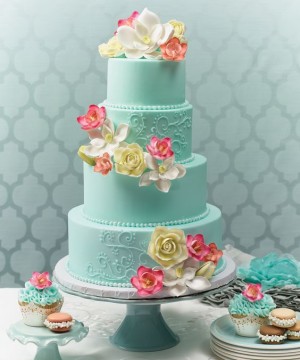 A stunning three-tiered cake with the best color combination for cake icing, accompanied by cupcakes, beautifully presented on a table for a Quinceanera celebration.