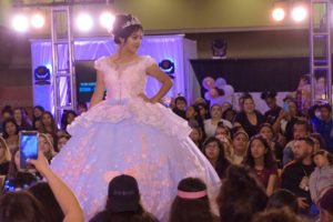 A woman wearing a Quinceanera gown walking down a stage during a fashion show