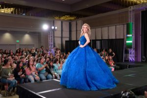 A woman in a blue dress walking on a runway showcasing fashion show Quinceañera dresses