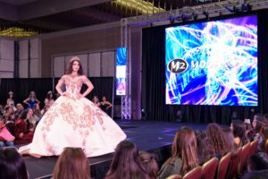 A woman in a white dress on a runway showcasing stage Quinceañera dresses