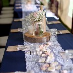 A Quinceanera reception with a navy blue rustic theme. The image shows a long table with a blue tablecloth and white place settings.