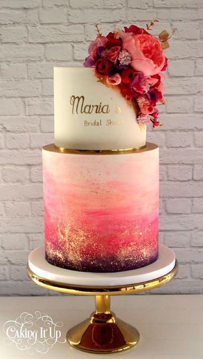 A pink and gold watercolor cake with three tiers and flowers on top