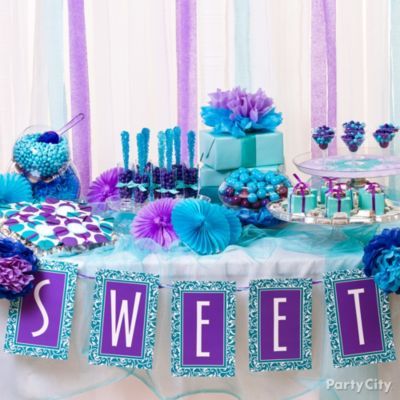 A Quinceanera party with a pink, blue, and purple birthday theme. The table is topped with lots of blue and purple decorations.