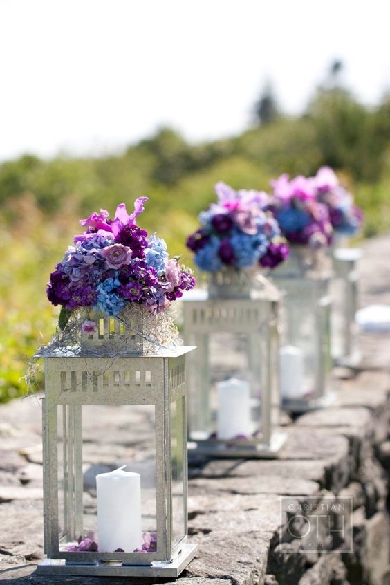 A group of purple and blue vases with flowers in them, along with a lantern for Quinceanera decoration