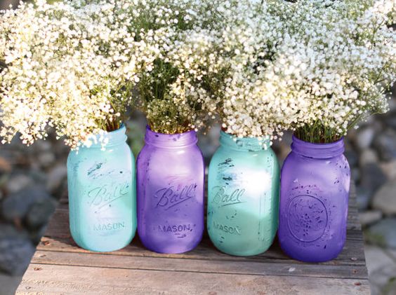 A row of four painted mason jars filled with baby's breath and lavender, perfect for a Quinceanera celebration.