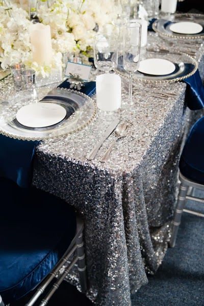 Quinceanera, a table with a navy and silver decor featuring a silver table cloth and blue chairs