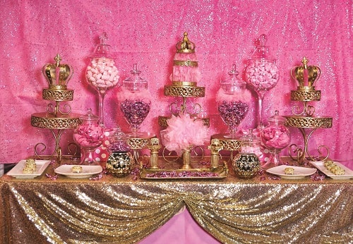 A tradition Quinceañera table topped with lots of candy covered in pink and gold