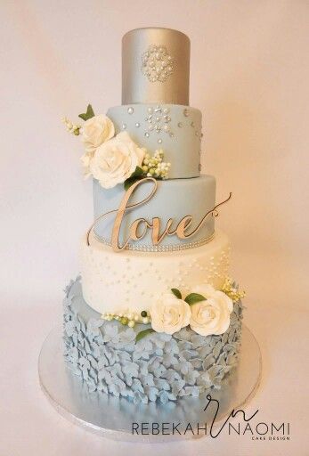 A beautiful gold and gray Quinceanera cake on a dining room table adorned with blue and white flowers