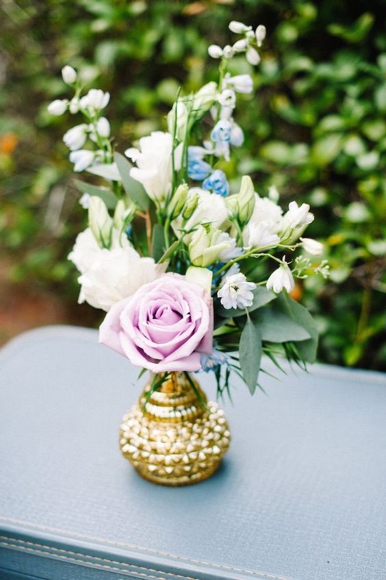 A beautiful floral arrangement of purple and white flowers in a gold vase, perfect for a Quinceanera celebration.