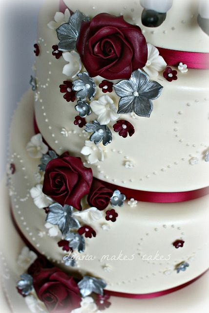 Close up of a silver and maroon Quinceanera cake with red roses and a Quinceanera invitation