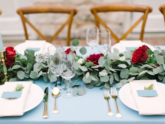 A Quinceanera centrepiece, featuring a blue tablecloth adorned with white plates, silverware, and a Quinceanera invitation.