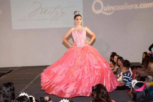 A fashion model walking down a runway in a pink Quinceañera dress