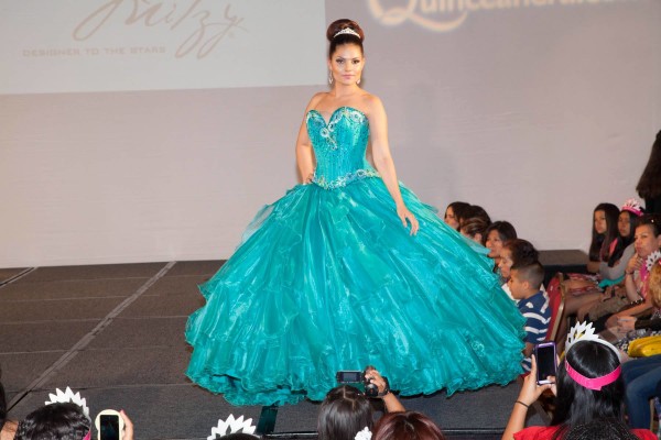 Quinceanera: A woman in a blue dress walking down a runway wearing a gown