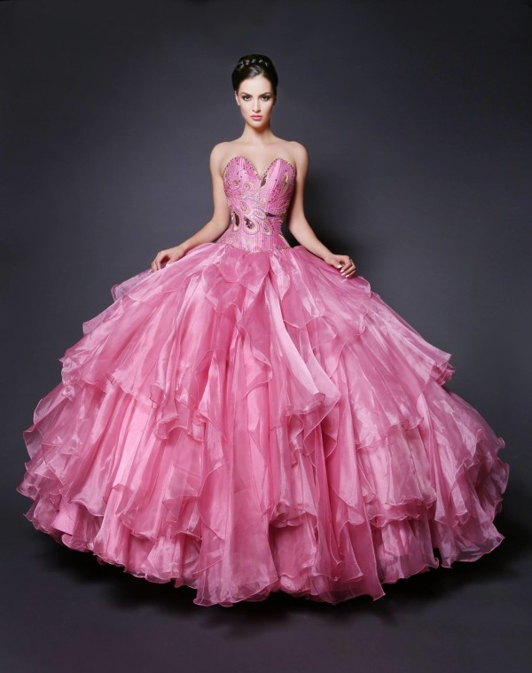 A woman in a pink ball gown posing for a picture at a Quinceanera event.
