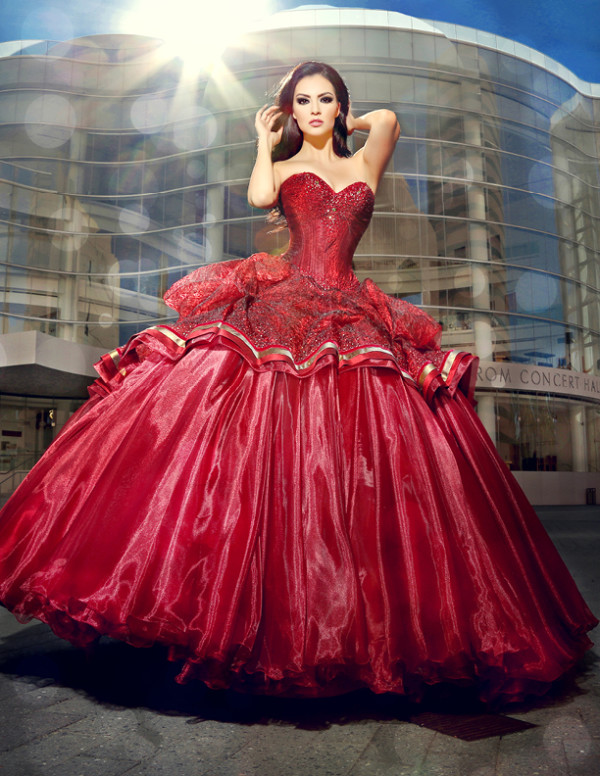 A woman in a red Quinceanera dress posing in front of the Segerstrom Center for the Arts.