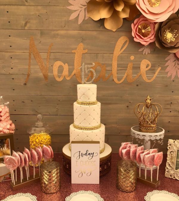A Quinceanera dessert table with a cake covered in pink and gold