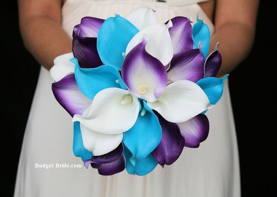 A woman in a white dress holding a blue and white bouquet with a floral design of blue and purple flowers in the background, perfect for a Quinceanera celebration.