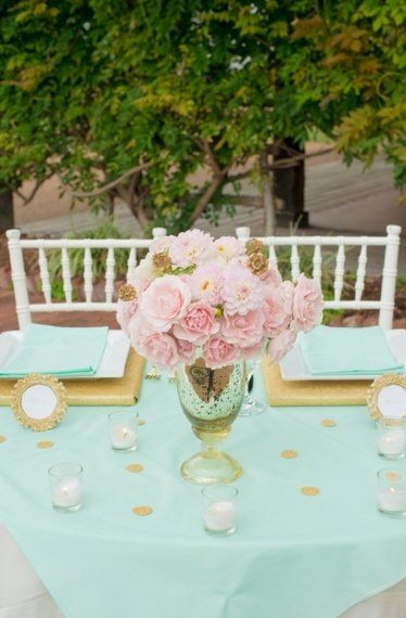 A Quinceanera invitation with mint green, pink, and gold decorations. A young woman holding a blue box with a pink bow.