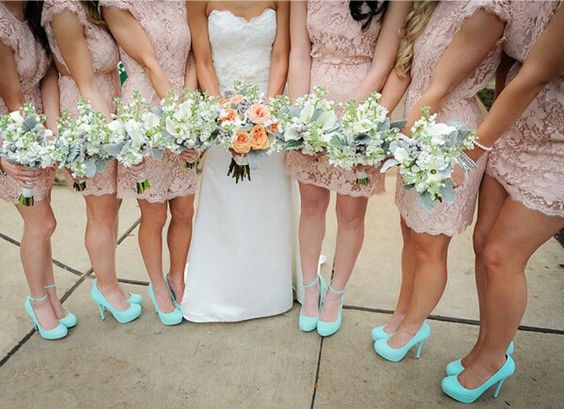 A group of bridesmaids at a Quinceanera celebration, dressed in peach dresses and holding bouquets of flowers. They are wearing blue shoes to match their dresses.
